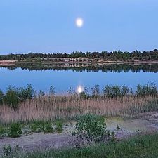 Blick auf einen See. Der Mond spiegelt sich in der Wasseroberfläche.