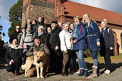  20 Frauen und Männer sowie ein Hund posieren vor einer Kirche.