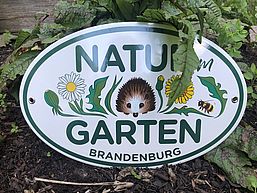Plakette mit Aufschrift Natur Garten Brandenburg und einem Igel zwischen Wiesenblumen