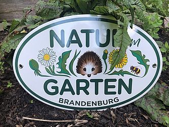 Plakette mit Aufschrift Natur Garten Brandenburg und einem Igel zwischen Wiesenblumen